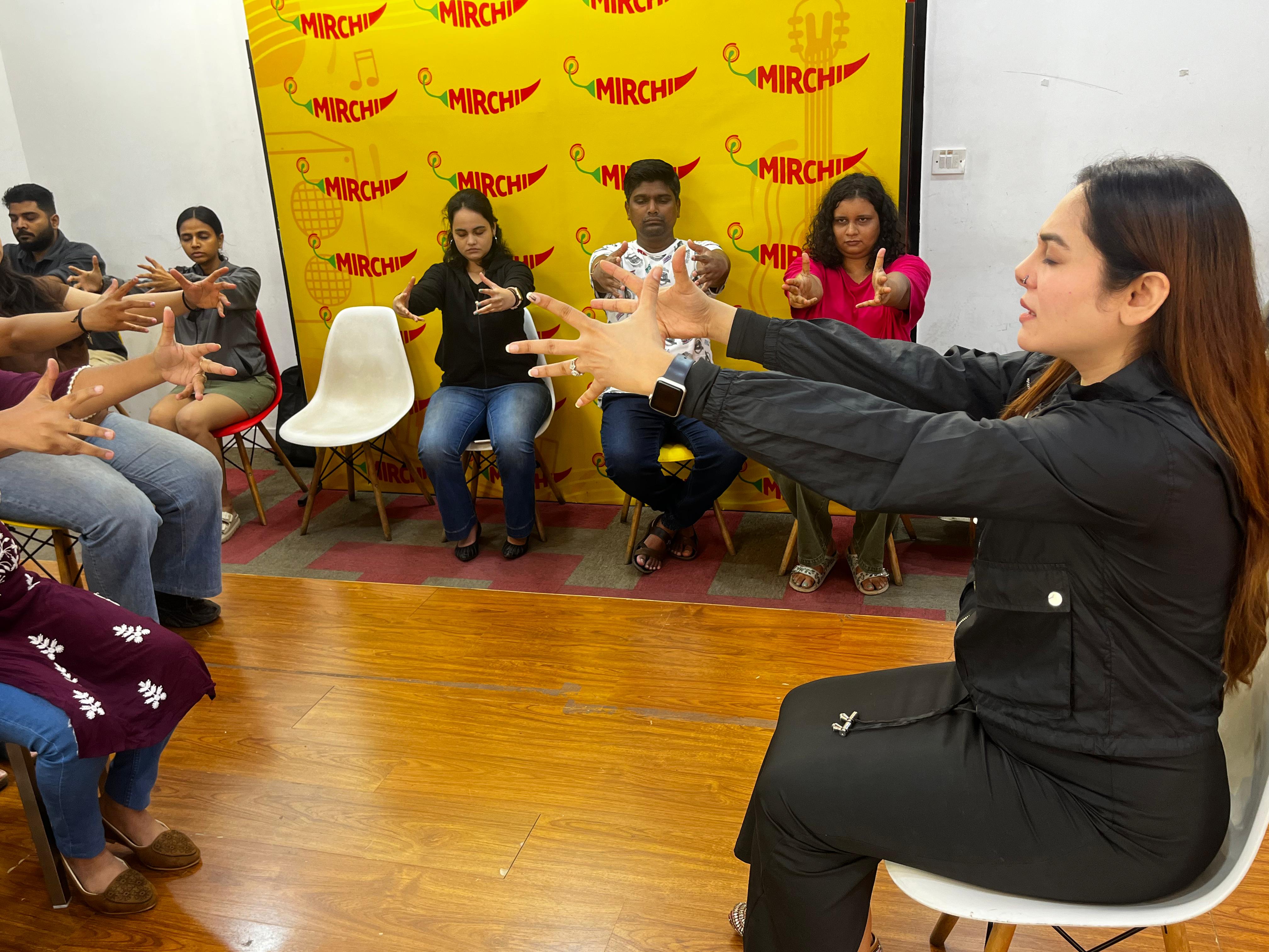 Vibha Jain seated in front of a group, leading participants through a hand and arm relaxation exercise.