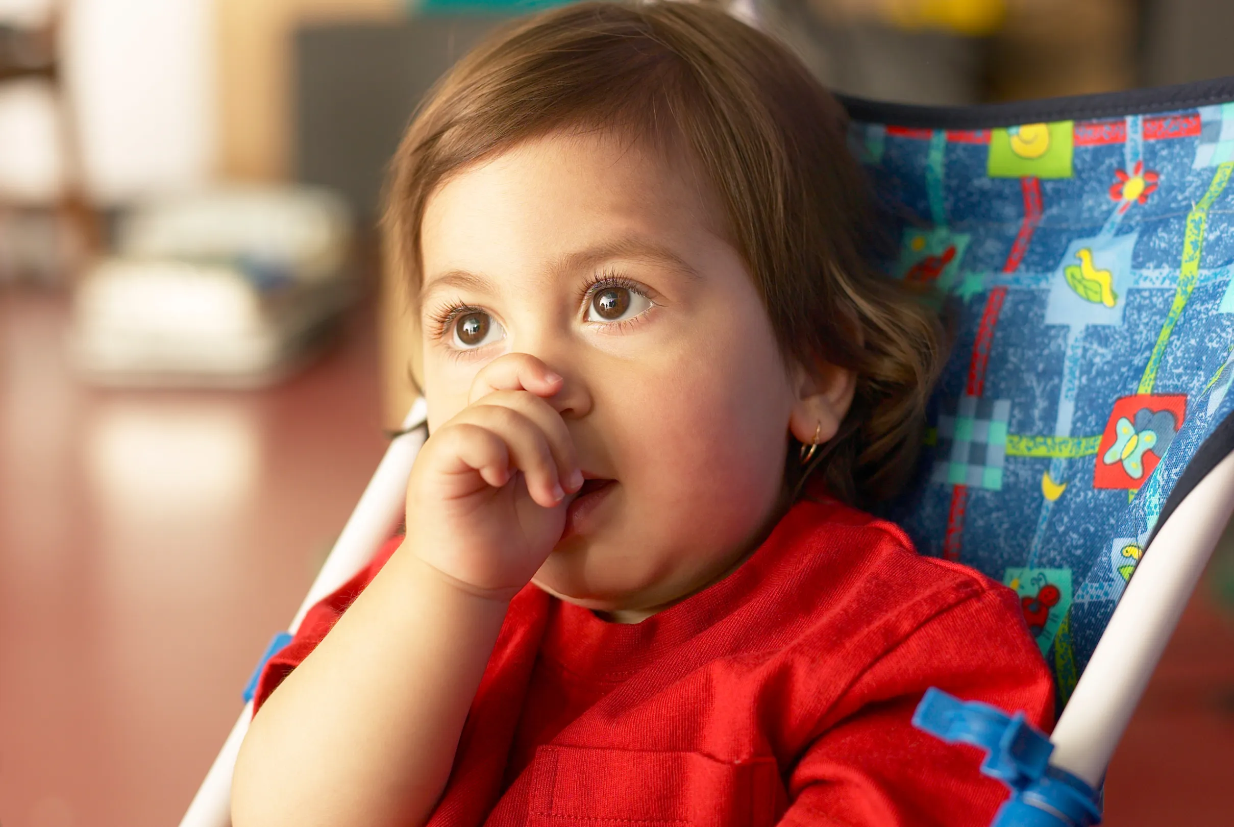 A relaxed young child sitting quietly with a thumb resting near the mouth.